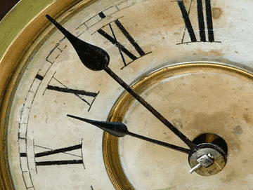 Close-up of antique clock face displaying Roman numerals with black hour and minute hands.